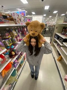 a woman carrying a teddy bear on her shoulders in a store aisle with shelves full of toys