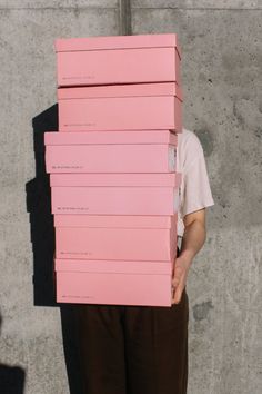 a person holding a stack of pink boxes on their head in front of a concrete wall