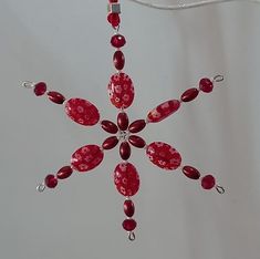 a red glass ornament hanging from a white string with beads and chains attached to it