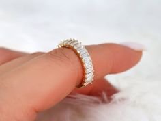 a woman's hand holding a diamond ring on top of white furnishing