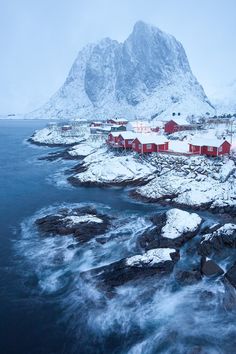 a red house sitting on top of a snow covered hill next to the ocean and mountains