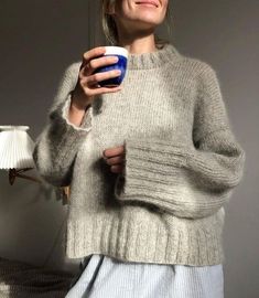 a woman holding a cup in her right hand and wearing a gray sweater on the left