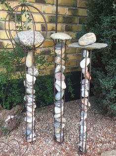 three metal sculptures made out of rocks in front of a brick wall and shrubbery