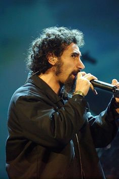 a man with long hair holding a microphone in his right hand and looking off to the side