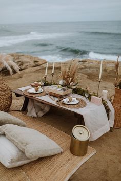 a table set up on the beach for an outdoor dinner party with candles and place settings