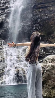 a woman standing in front of a waterfall with her arms outstretched out to the side