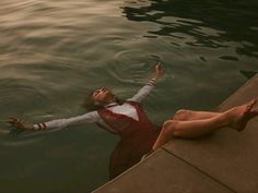 a woman floating on top of a body of water next to a dock with her arms outstretched