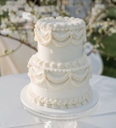 a three tiered white wedding cake sitting on top of a glass plate covered in frosting