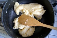 a wooden spoon in a black pan filled with mashed cauliflower and butter