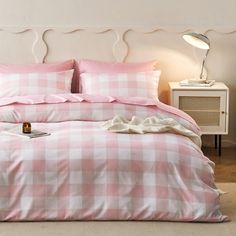 a pink and white checkered comforter set on a bed in a room with a lamp