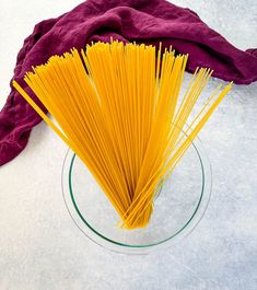 a glass bowl filled with yellow noodles on top of a white tablecloth next to a red towel