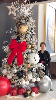 a woman standing next to a christmas tree with ornaments on it and a red bow