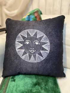 a black pillow with a sun design on it sitting on a green chair next to a stuffed animal