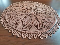 a crocheted doily sits on a wooden table, ready to be used as a placemat