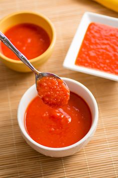 a spoon full of tomato sauce with another bowl in the background