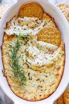 a casserole dish with crackers, cheese and herbs in it on a table