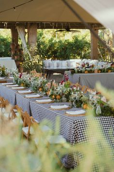 an outdoor dining area with tables and chairs covered in plaid cloths, surrounded by greenery