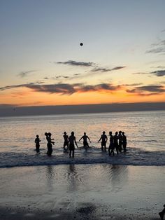 a group of people standing on top of a beach next to the ocean at sunset