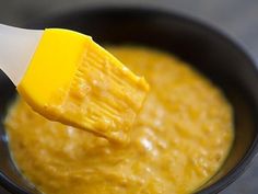 a yellow spatula being used to dip cheese into a sauce in a black bowl