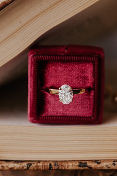 an engagement ring in a red velvet box on top of a wooden table with books