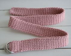 a pink crocheted belt with a metal ring on the end is laying on a white wooden surface