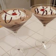 two martini glasses filled with ice cream and chocolate sauce on a white tiled counter top