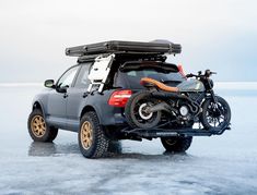 an suv with two bikes on the back parked in ice covered water next to a motorcycle