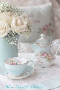 white roses in a teacup and saucer on a table next to a pillow