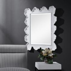 a white mirror sitting on top of a table next to a gray chair and ottoman