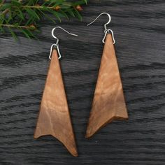 the wooden earrings are hanging from silver earwires on a black background with pine needles