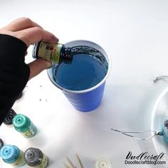 someone pouring blue liquid into a cup with pins and thread on the table next to it