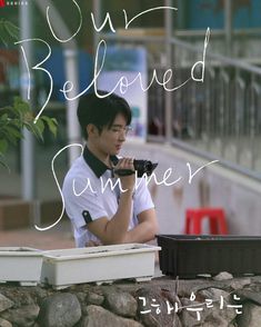 a man holding a camera next to a rock wall with the words our beloved summer written on it