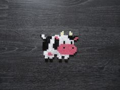 a cross stitch cow is shown on a black surface with white and pink dots in the shape of a cow's head