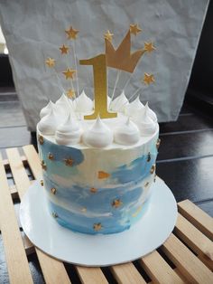 a blue and white birthday cake with gold stars on top, sitting on a wooden table