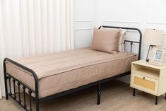 a bed with a metal frame next to a night stand and lamp on a wooden floor