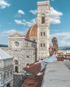 a woman sitting on top of a roof next to a tall building with a cathedral in the background