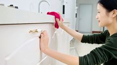 a woman cleaning the side of a white cabinet