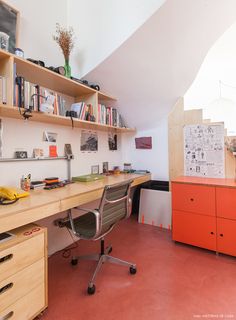 a room with a desk, chair and shelves filled with books on top of it