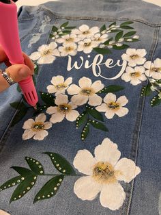 someone is painting flowers on the back of a jean jacket that says,'wife '