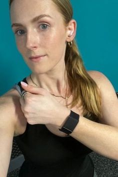 a woman sitting in front of a blue wall with her hand on her wrist and looking at the camera