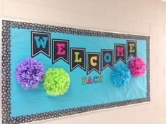 a welcome sign with pom poms hanging on the wall in front of it