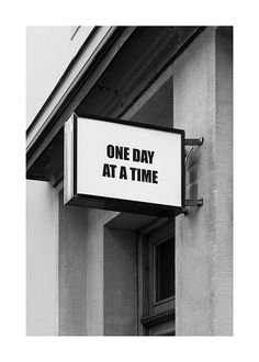 a one day at a time sign hanging off the side of a building in black and white