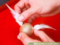 a person is holding an egg with white feathers and gold paint on it, while another hand holds one