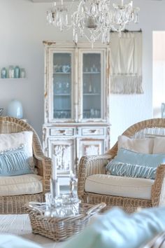 two wicker chairs sitting next to each other in front of a white cabinet and chandelier