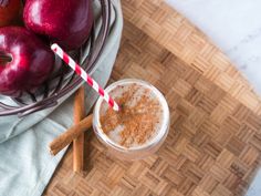 an apple smoothie with cinnamon sticks and two apples in the background on a cutting board