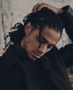 a man with dreadlocks is holding his hair in one hand and looking down