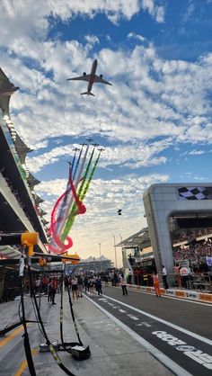 an airplane is flying in the sky over a race track with people watching from the sidelines