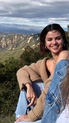 two young women sitting on the side of a hill smiling and looking at the camera