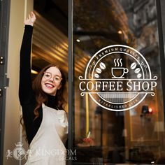 a woman standing in front of a coffee shop holding her arms up to the window