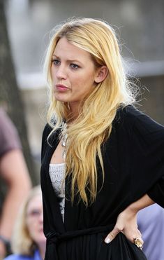 a woman with long blonde hair is standing in front of people and looking at the camera